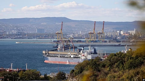 Cargo ships docked at a busy port with cranes and a city in the background.