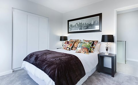 A neatly arranged bedroom with a double bed and colorful pillows.
A framed cityscape hangs on the wall above the bed.