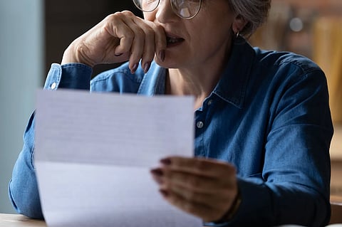 The image shows a woman in a denim shirt holding a paper and appearing stressed or worried while reading it.
