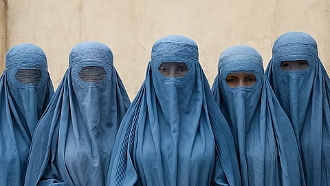 The image shows four women wearing blue burqas that cover them completely, with mesh panels over their eyes.