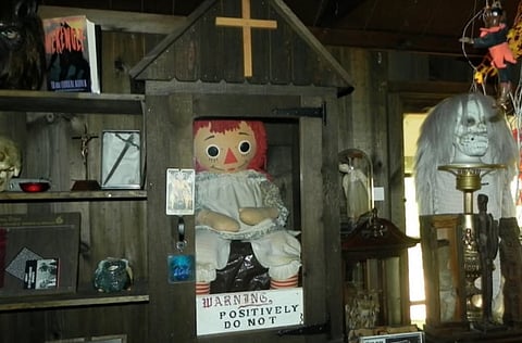A doll sits inside a wooden box, which has a sign attached to it, indicating its purpose or name.