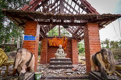A damaged Buddhist temple with a statue draped in orange cloth surrounded by debris.