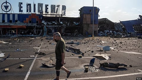 A boy walks through a shattered street filled with debris in front of a burned, ruined building.