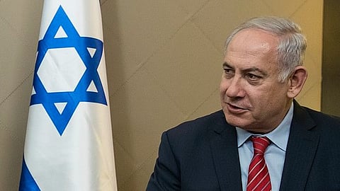 The image shows an older man in a suit sitting beside an Israeli flag with a blue Star of David.