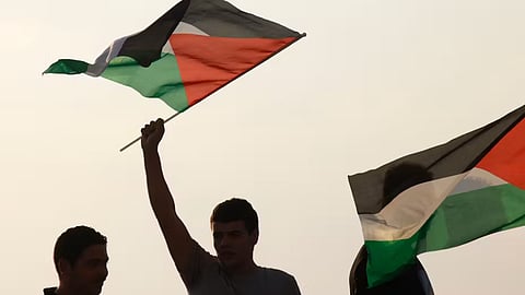 3 people raising the Palestinian flag up in the sky.