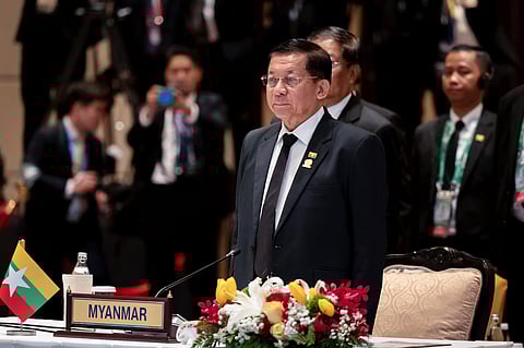 The image showcase Myanmar's military leader in a press conference or a meet he is wearing formals and addressing some people. many other are standing behind him wearing formals