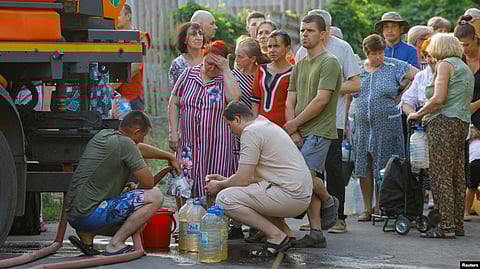 In the image residents are waiting in line to collect water 
