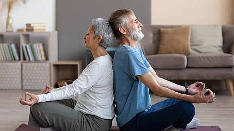 An old couple meditating with backs opposite to each other.