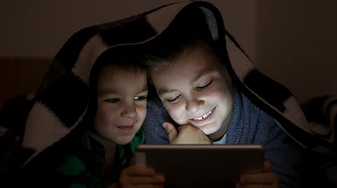 Kids under blanket seeing tablet