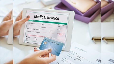 A person holding a tablet displaying a “Medical Invoice” form while using a blue credit card for payment. The scene suggests an online medical bill payment process, with papers and office items visible on the table.