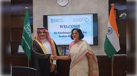 Khalil bin Ibrahim bin Salamah and  Nivedita Shukla Verma shake hands. Behind them, Saudi and Indian flags stand beside a welcome sign, creating a formal and friendly atmosphere.