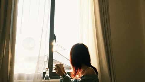 A girl drinking tea and looking outside the window with the morning sunlight
