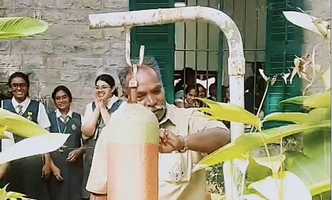 The peon uncle standing in front of bell looking at his watch to see the time and all the children in the background happy shouting cheering for him as he rang his last bell