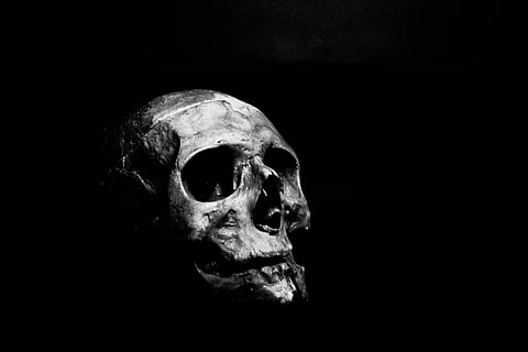 An image of a dark room with human skull in the centre. The image is black and white