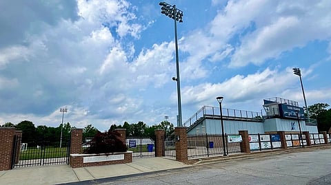 Blue clear over the playground and field of a christian school. The gates are closed and there is an area outside the gate before the starting of the streets.