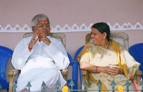 Image of Lalu Yadav and his wife Rabri devi sitting on a chair. Rabri devi is looking at the former railway minister with a smile on her face.