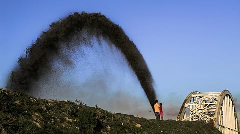 Two boys standing and watching crude oil fountain in a field.