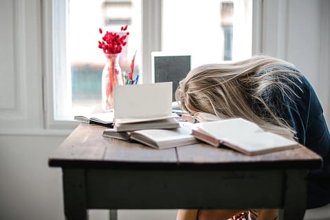 In the image a girl is shown in her study table with her head down to represent confusion and books around her are open