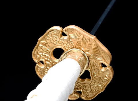 Close up shot of a Japanese sword with a golden design and white handle.