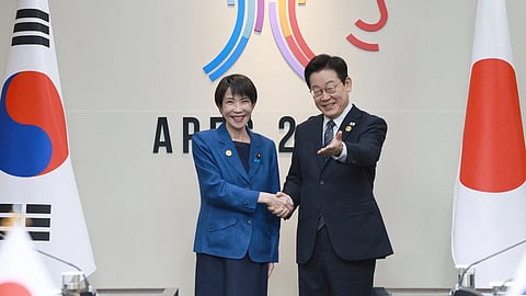 South Korean President Lee Jae-Myung and Japanese Prime Minister Sanae Takaichi shaking hands at a high-level summit. The flag of the respectives countries are at their sides