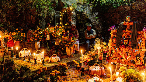 Vibrant Day of the Dead altar in evening light at Mexico, it is decorated with flowers and candles giving it a golden glow. 