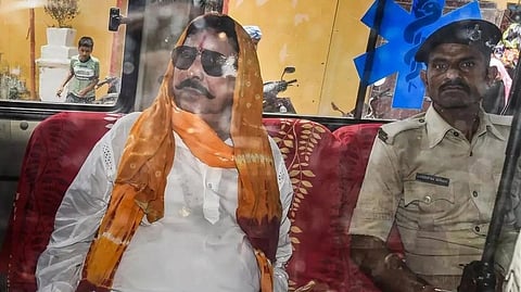 In the image Anant singh is seen in a police van beside a police officer. The photo is taken from outside car mirror