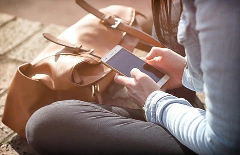 Image of a woman sitting with her phone in her hands. She has got her  brown handbag right in  front of her. 