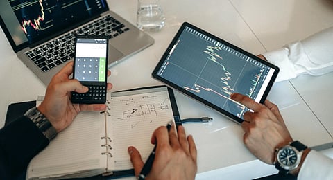 Image of two men analysing data on a digital tablet. There are pen, laptop and diary.
