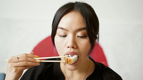 A girl eating sushi food with chopsticks