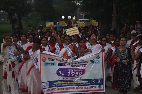 Women in Paliganj constituency march for voter awareness, with a banner showing the voter helpline number, 1950.