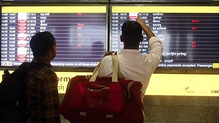 Busy terminal of Indira Gandhi International Airport in Delhi with delayed flights displayed on departure boards, after an air-traffic-control system failure. There are two individual looking at the display board while carrying their bags.