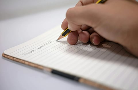 Image of A Person Writing on a Journal with a yellow black designed pencil 
