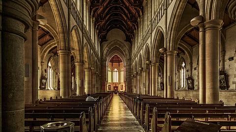 Interior view of a brown concrete cathedral featuring elegant seating areas and a magnificent, intricately designed ceiling.