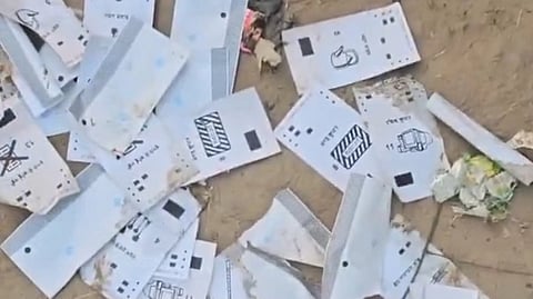 Torn and discarded ballot papers scattered on the ground, showing various election symbols and markings, suggesting possible mishandling or damage during an election process.