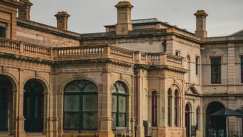 Werribee Park Mansion in Australia. A concrete old mansion with green lawn and benches in the front.