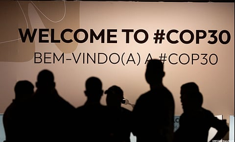 In the image the UN Climate conference board is shown with "Welcome to #COP30" written in it and the shadow of people upon it