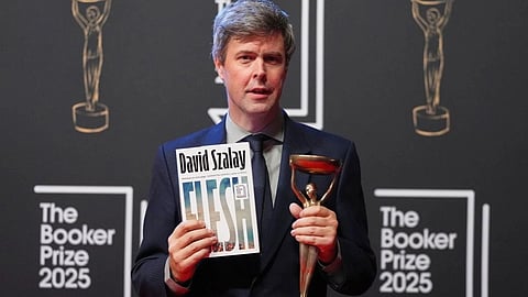 In the image David Szalay is showing his Book Flesh and his award to the camera in th Booker prize 2025 stage