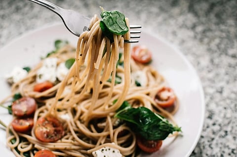 A fork lifts spaghetti with spinach and halved cherry tomatoes over a white plate. The dish includes mozzarella chunks, creating a fresh, appetizing look.