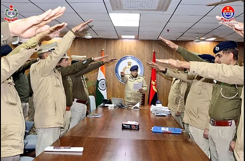 Gurugram Police officers raising their right arms in a salute during a meeting.