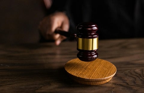  A hand holds a wooden gavel poised above a round sound block on a polished wooden table, conveying a sense of authority and decision-making.