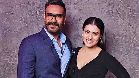 In the image Ajay Devgan and Kajol are shown smiling at the camera