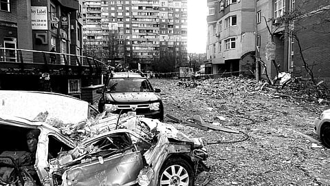 Debris-strewn street with two damaged cars, one severely crushed, surrounded by scattered rubble and broken buildings, conveying destruction and chaos.