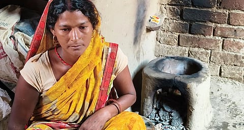 A woman sitting with a wood stove behind her.