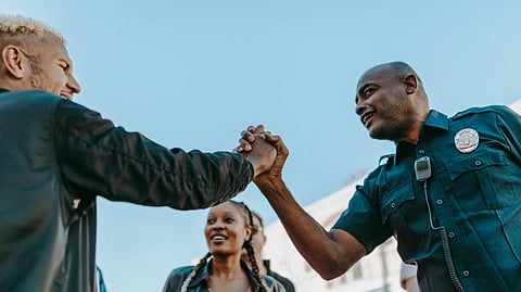 Two people holding hands warmly in a friendly, cheerful setting, with a girl with braided hair smiling in the background.