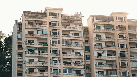 Tall, weathered apartment building with multiple balconies. The foreground shows older, rustic rooftops, creating a contrast against the modern high-rise.