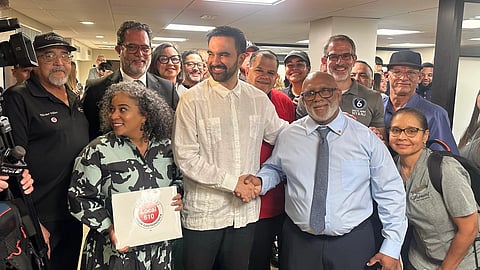 Zohran Mamdani posing with a labour union in New York. He is standing in the centre, shaking hands with a man.