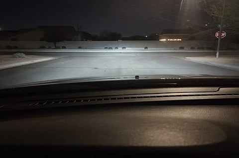 View from a car dashboard at night, headlights illuminating a residential street. A stop sign is visible on the right. The mood is calm and quiet.