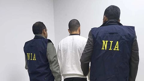 Anmol Bishnoi with his back to the camera in a white tshirt with NIA officers on both sides.