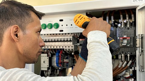 A man wearing a full sleve white tshirt is working on an electrical panel.