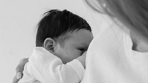 A mother lovingly cradles her baby close to her chest. The baby, dressed in a soft, white onesie, appears calm and content. The monochrome tones add a serene and intimate feel.